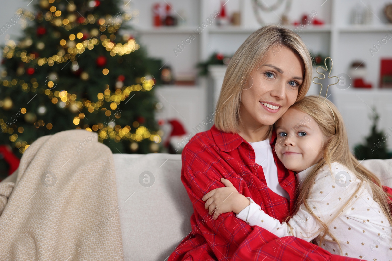 Photo of Cute little girl with her mom on sofa against Christmas lights. Space for text