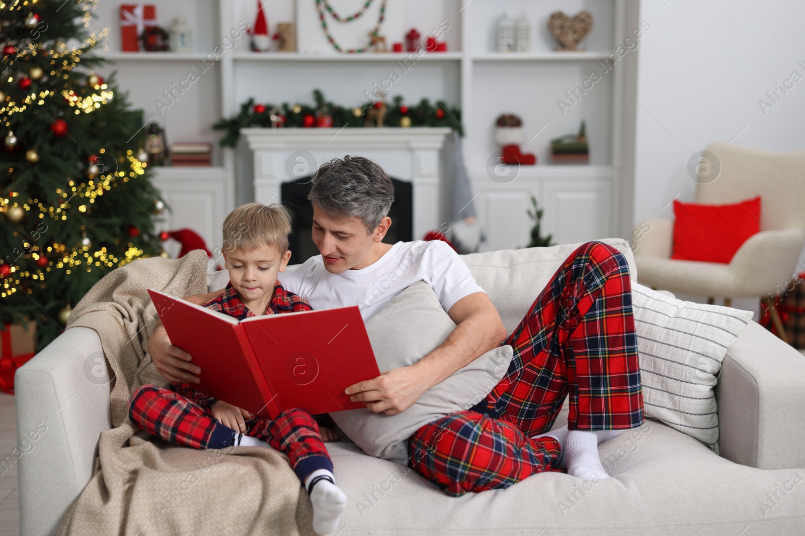 Photo of Father and son reading book together on sofa at home. Christmas holidays