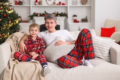 Photo of Father and son in pajamas on sofa at home. Christmas morning