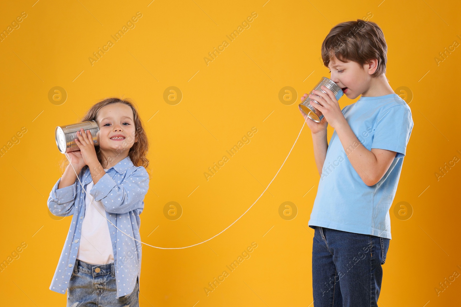 Photo of Boy and girl talking on tin can telephone against orange background