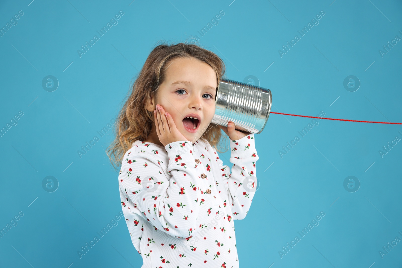 Photo of Surprised girl using tin can telephone on blue background