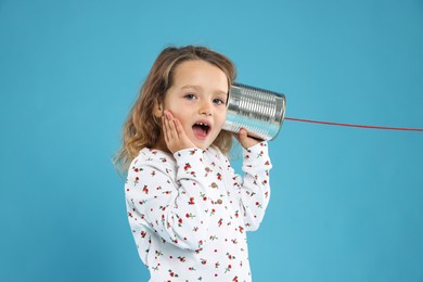 Photo of Surprised girl using tin can telephone on blue background