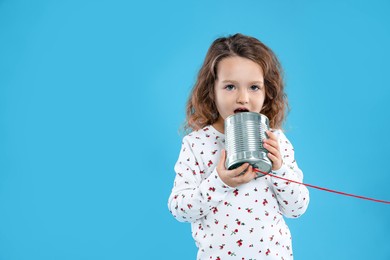 Girl using tin can telephone on blue background. Space for text