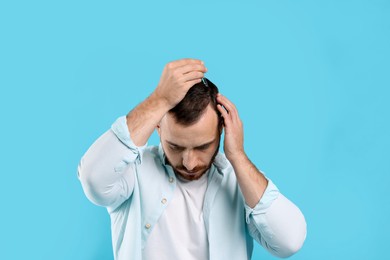 Photo of Baldness treatment. Man applying serum onto hair on light blue background