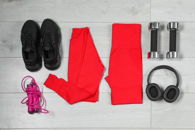 Photo of Stylish sportswear, black sneakers, dumbbells, skipping rope and headphones on wooden background, flat lay