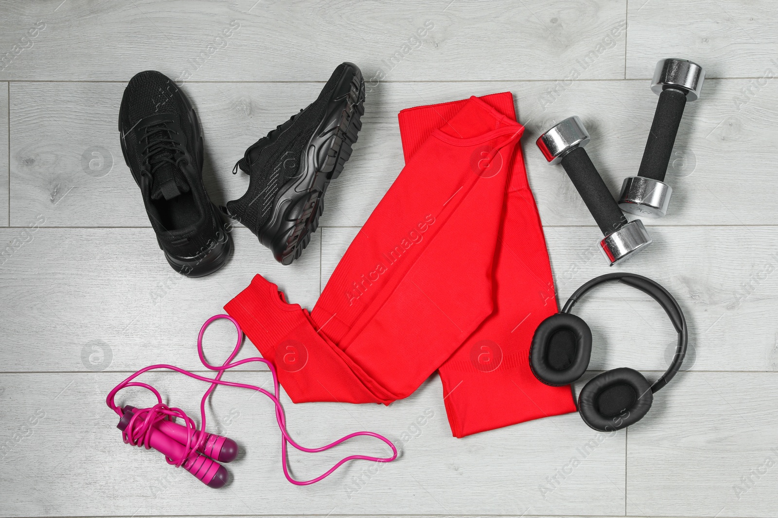 Photo of Stylish sportswear, black sneakers, dumbbells, skipping rope and headphones on wooden background, flat lay