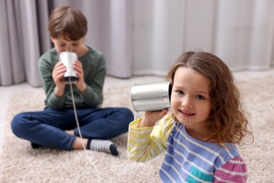 Boy and girl talking on tin can telephone indoors, selective focus