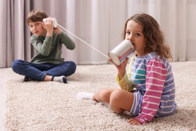 Photo of Boy and girl talking on tin can telephone indoors, selective focus