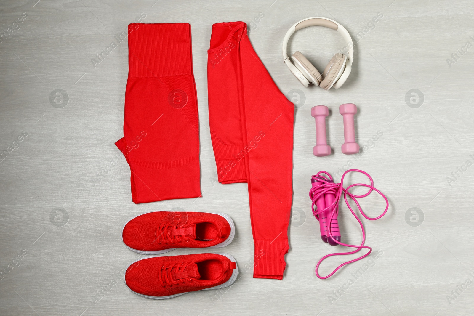 Photo of Stylish sportswear, red sneakers, dumbbells, skipping rope and headphones on wooden background, flat lay