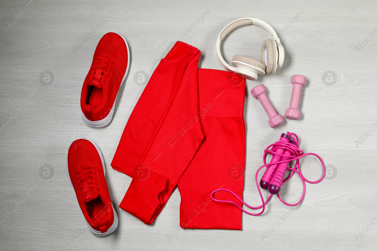 Photo of Stylish sportswear, red sneakers, dumbbells, skipping rope and headphones on wooden background, flat lay