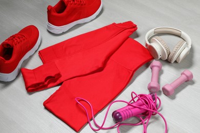 Photo of Stylish sportswear, red sneakers, dumbbells, skipping rope and headphones on wooden background, closeup