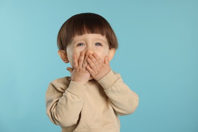 Photo of Portrait of emotional little boy covering mouth on light blue background