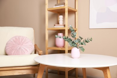 Photo of Stylish coffee table with eucalyptus near armchair at home