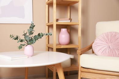 Photo of Stylish coffee table with eucalyptus near armchair at home