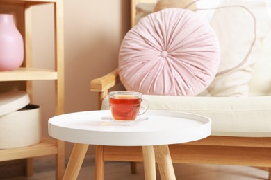 Photo of Coffee table with tea near armchair at home