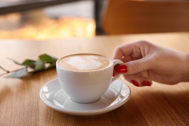 Photo of Woman with cup of aromatic coffee at wooden table in cafe, closeup