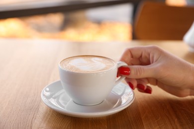 Photo of Woman with cup of aromatic coffee at wooden table in cafe, closeup