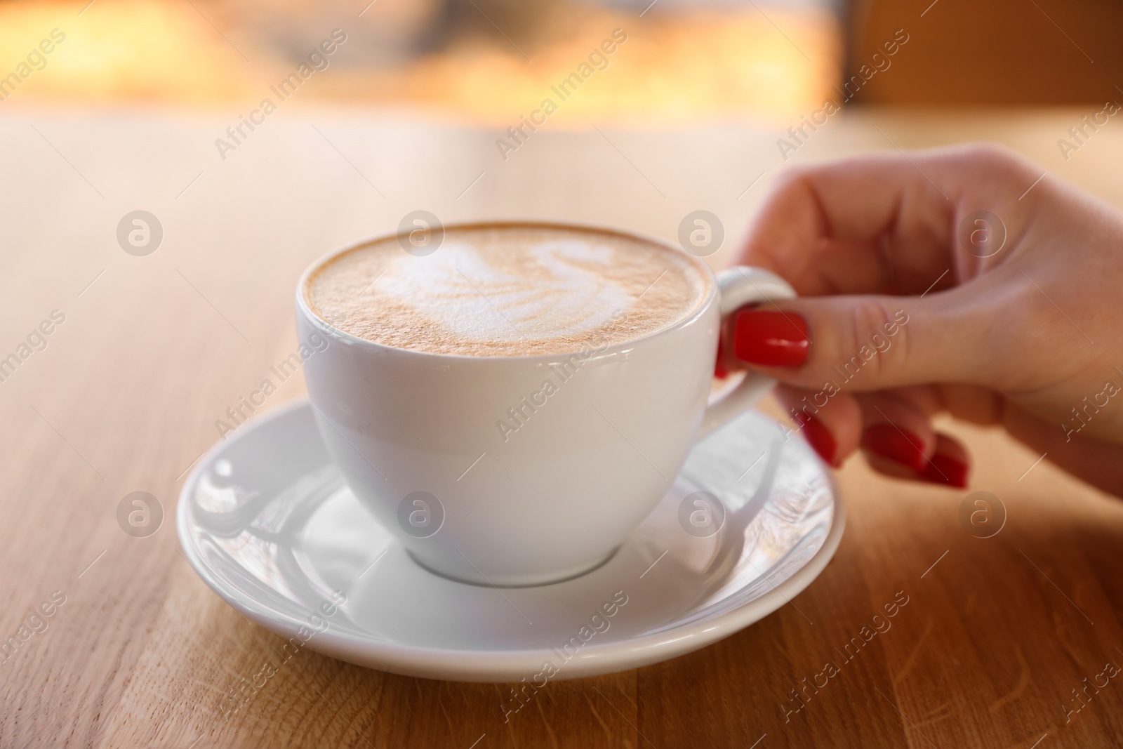 Photo of Woman with cup of aromatic coffee at wooden table in cafe, closeup