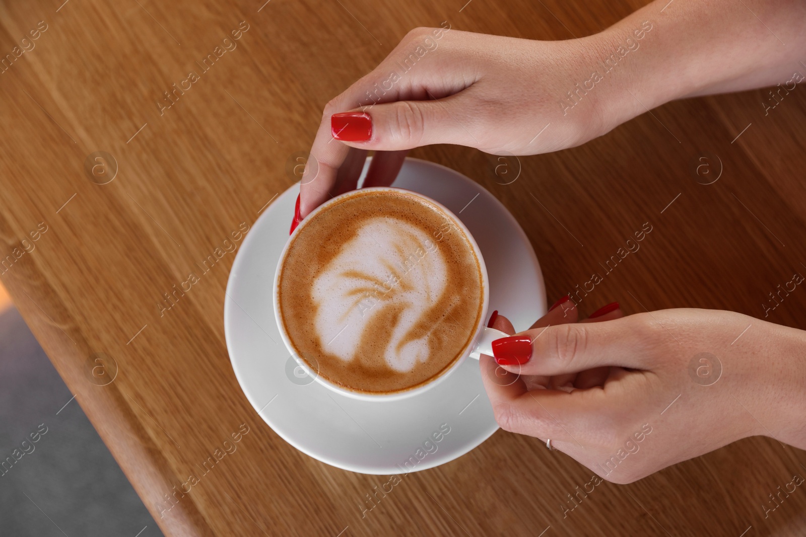 Photo of Woman with cup of aromatic coffee at wooden table in cafe, top view