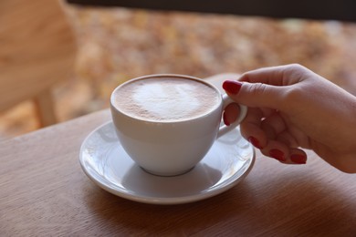 Photo of Woman with cup of aromatic coffee at wooden table in cafe, closeup