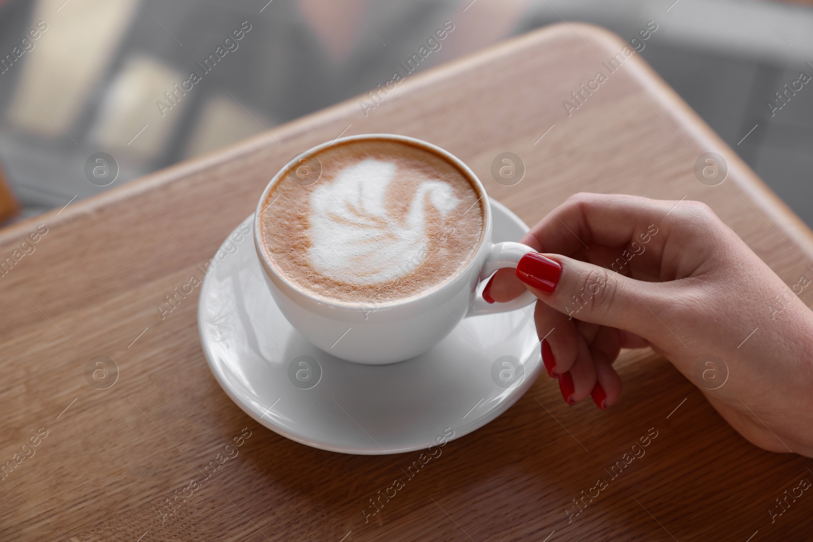 Photo of Woman with cup of aromatic coffee at wooden table in cafe, closeup