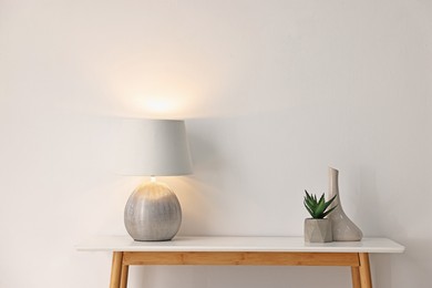 Photo of Stylish console table with lamp and decor near white wall indoors. Space for text