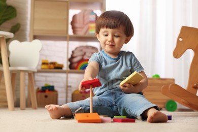 Photo of Cute little boy playing with toy pyramid on floor at home