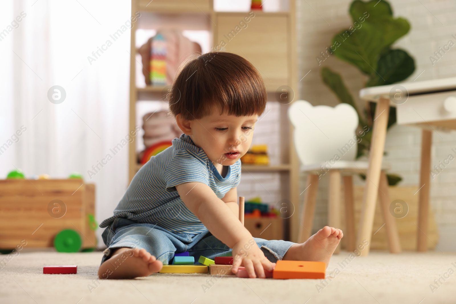 Photo of Cute little boy playing with toy pyramid on floor at home