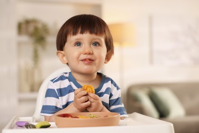 Photo of Cute little boy eating healthy food in high chair at home