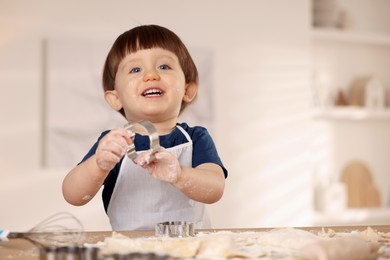 Photo of Cute little boy with cookie cutter at table indoors, space for text