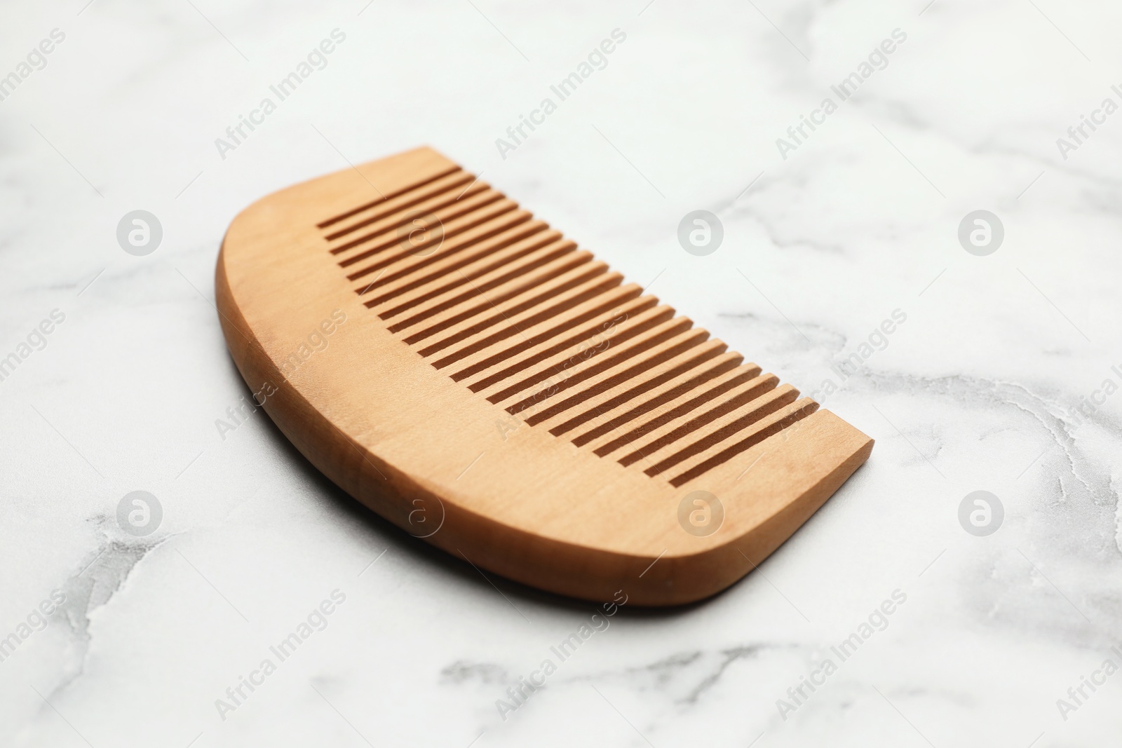 Photo of One wooden hair comb on white marble table, closeup