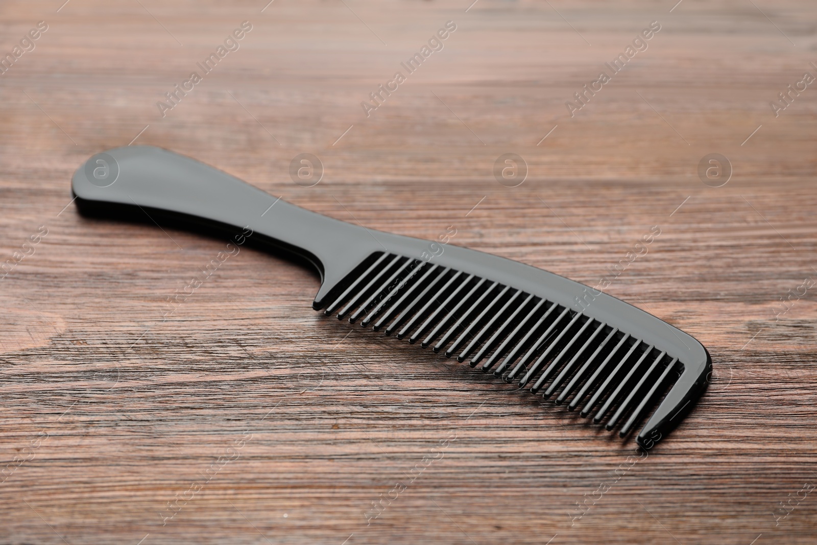 Photo of One black plastic comb on wooden table, closeup