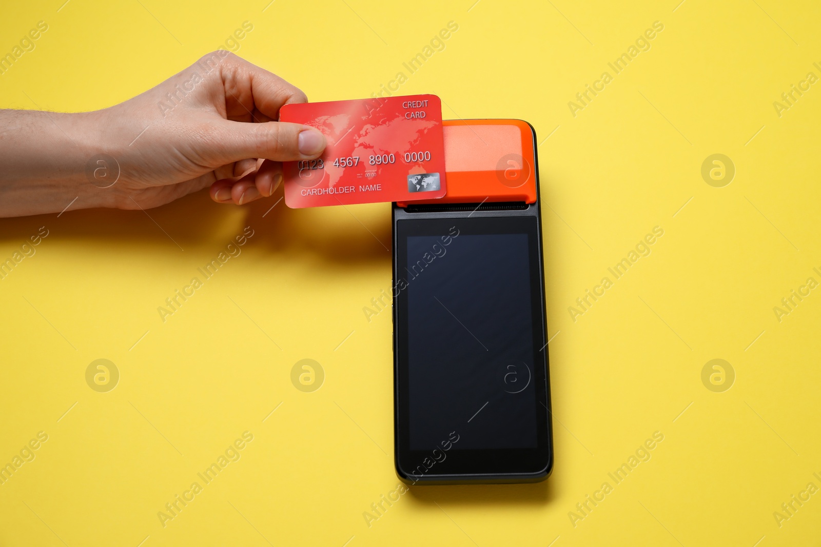 Photo of Woman with credit card using payment terminal on yellow background, top view