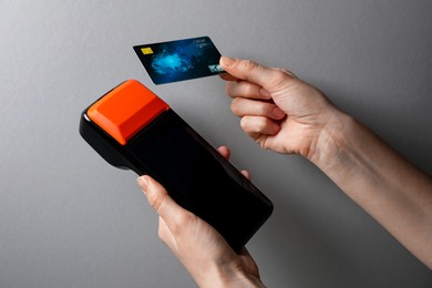 Photo of Woman with credit card using payment terminal on grey background, closeup