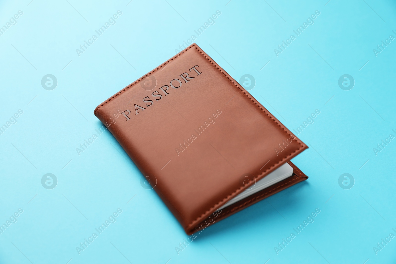 Photo of Passport in brown cover on light blue background, closeup