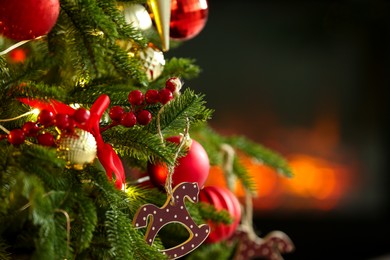 Photo of Beautiful Christmas tree decorated with horse toy, other ornaments and festive lights indoors, closeup. Space for text