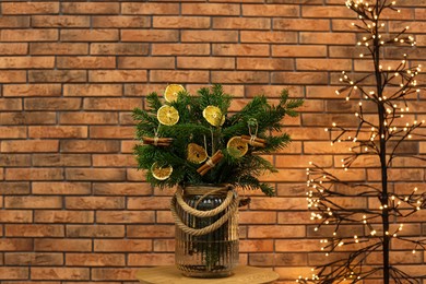 Photo of Beautiful fir tree branches decorated with dried orange slices and cinnamon sticks on table near Christmas tree lights