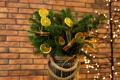 Photo of Beautiful fir tree branches decorated with dried orange slices and cinnamon sticks in vase against Christmas lights