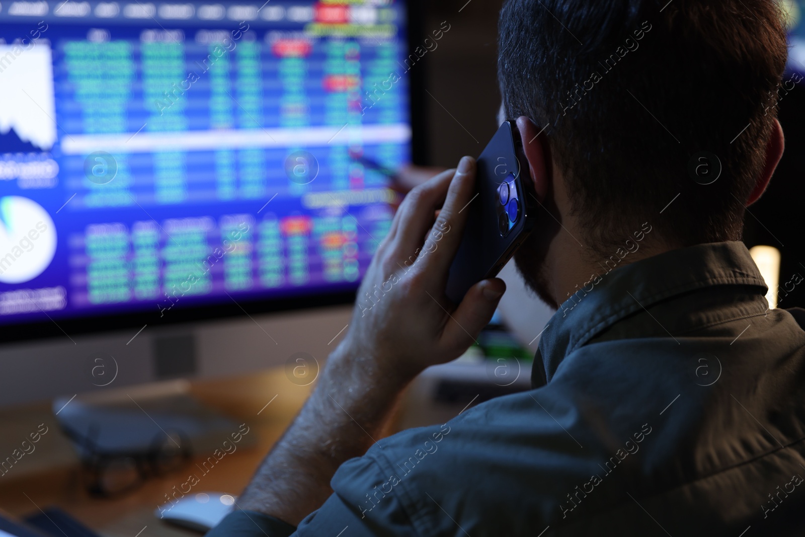 Photo of Financial trading specialist talking on phone in office at night, back view