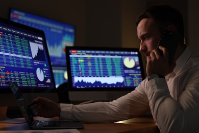 Photo of Financial trading specialist talking on phone in office at night