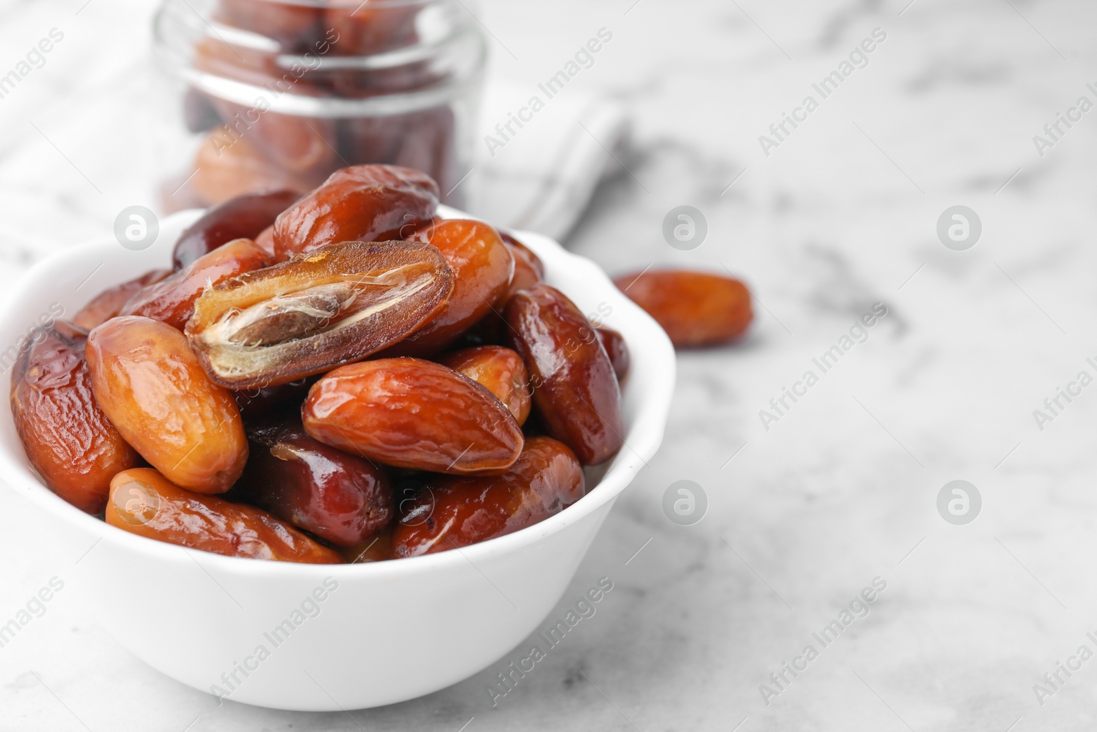 Photo of Tasty dried dates in bowl and jar on white marble table, closeup. Space for text