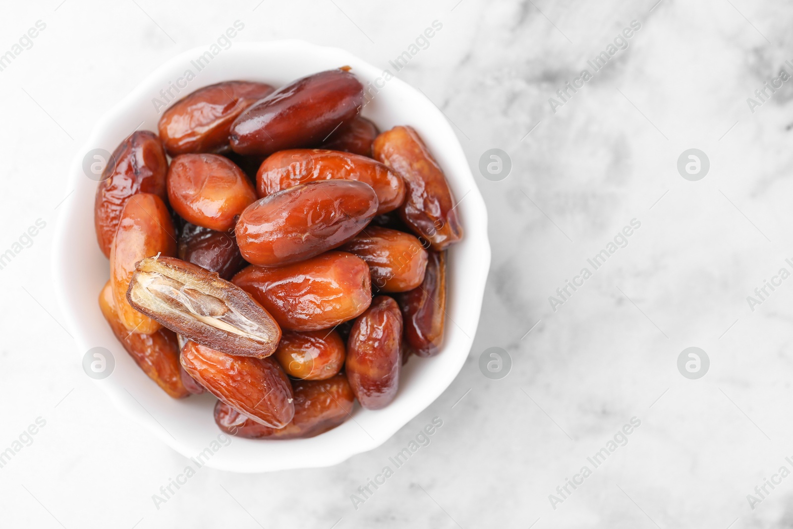 Photo of Tasty dried dates in bowl on white marble table, top view. Space for text