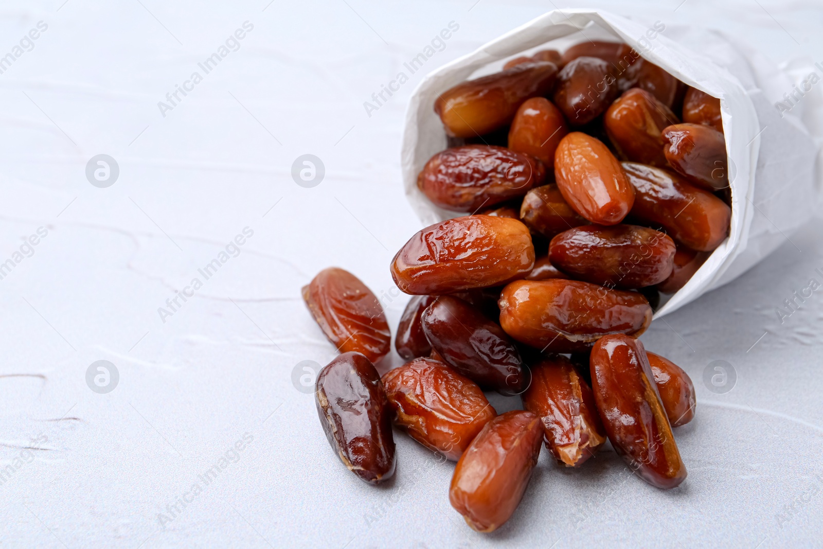 Photo of Tasty sweet dried dates in paper bag on white table, closeup. Space for text