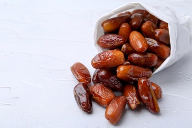 Photo of Tasty sweet dried dates in paper bag on white table, closeup. Space for text