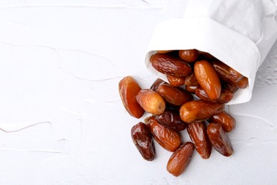 Photo of Tasty sweet dried dates in paper bag on white table, top view. Space for text