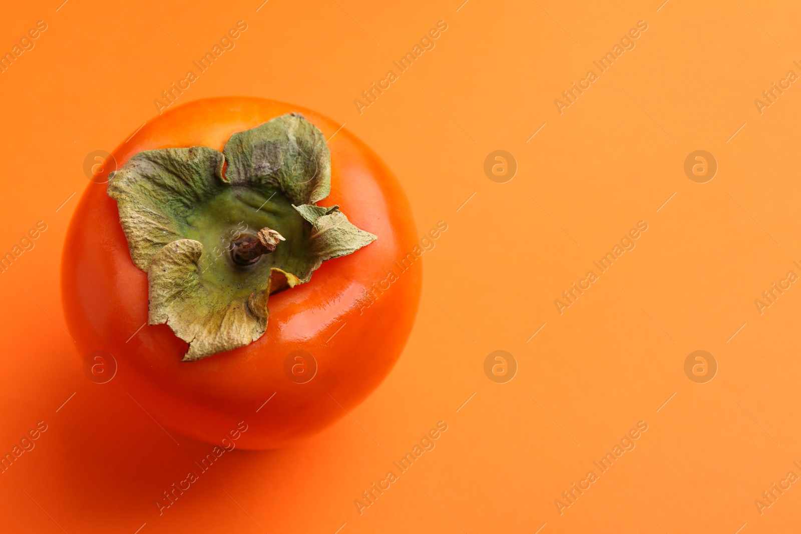 Photo of Delicious fresh juicy persimmon on orange table, closeup. Space for text