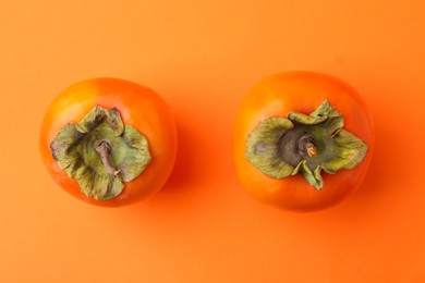 Delicious fresh juicy persimmons on orange table, flat lay