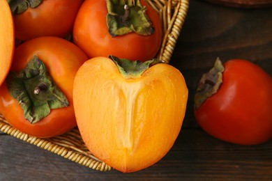 Photo of Whole and cut fresh persimmons in wicker basket on wooden table, top view