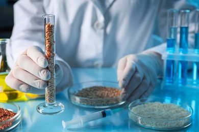 Photo of GMO concept. Scientist holding test tube with cereal grains at table in laboratory, closeup