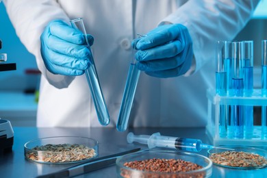 Photo of GMO concept. Scientist holding test tubes of liquid at table with different cereal grains in laboratory, closeup